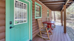 A wooden cabin with a turquoise door, a porch with a table and rocking chairs, and a covered area with a wooden ceiling. - Broken Bow 'starlight Cabin' w/ Private Hot Tub! (Broken Bow)