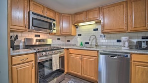 A kitchen with wooden cabinets, stainless steel appliances, a microwave, stove, oven, dishwasher, and a tiled backsplash. - Rustic & Modern Russell Cabin w/ Grill + Deck (Russell)