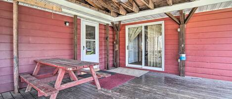 Un patio cubierto con una mesa y bancos de madera, un muro exterior rojo y techo de madera.