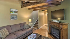 Ein Wohnzimmer mit Kamin, einer Couch, einem Fernseher und einer Treppe zu einer oberen Ebene.