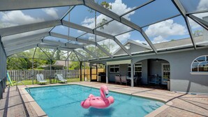 En pool med tak och en rosa uppblåsbar flamingofigur, en uteplats med stolar och en utsikt över ett hus i bakgrunden.