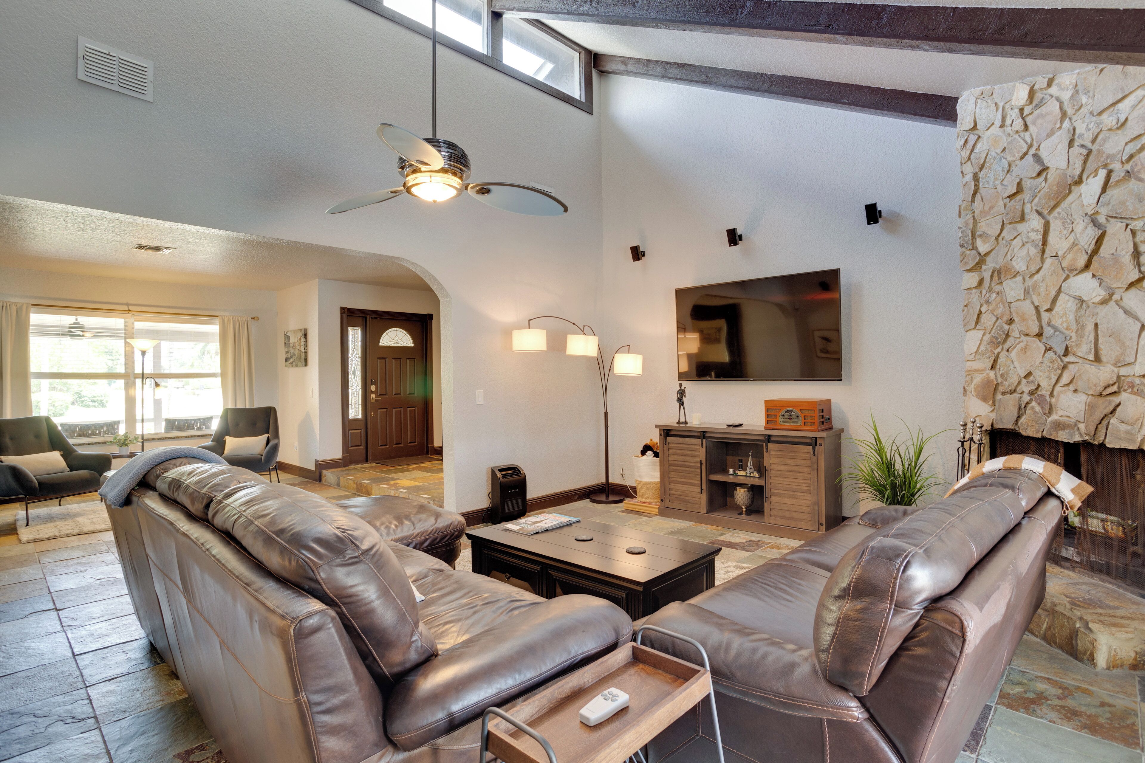 A spacious living room with leather sofas, a coffee table, and a stone fireplace.