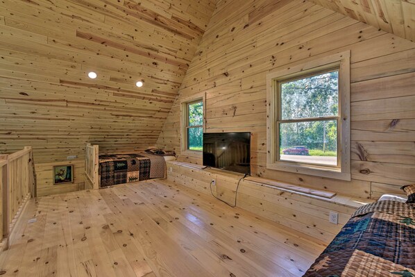 Une cabane aux murs et au plancher en bois, avec une cheminée, une grande fenêtre et un escalier.