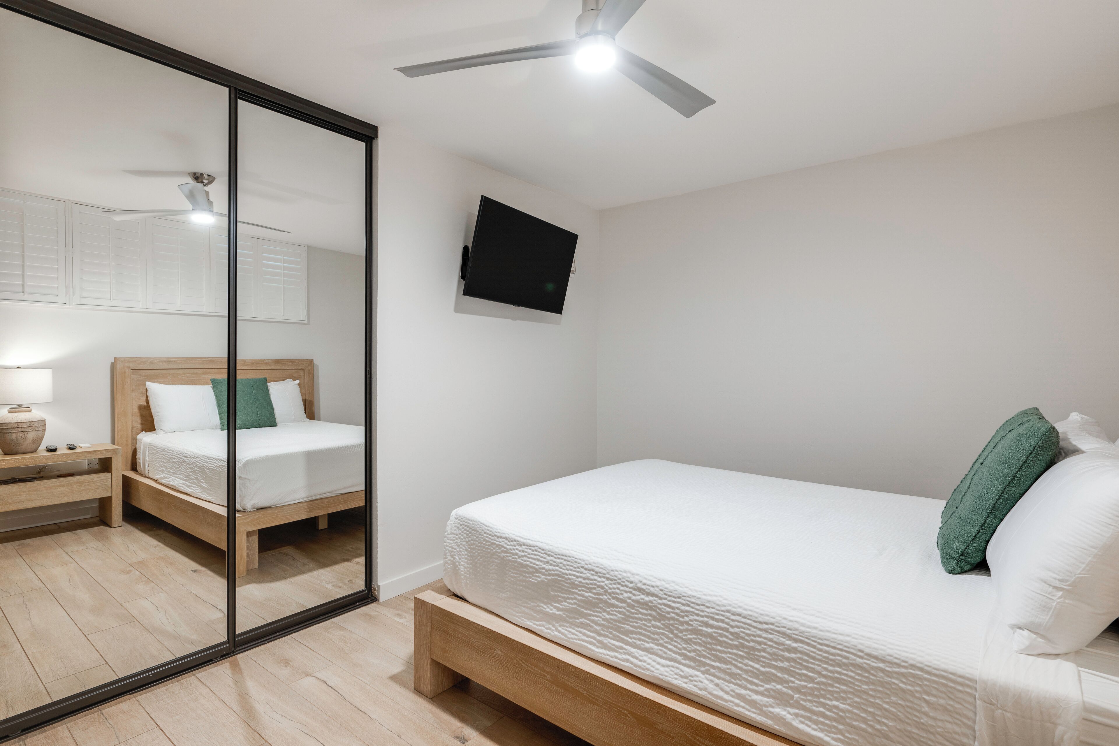 A bedroom with a bed, bedside table, lamp, and a ceiling fan.