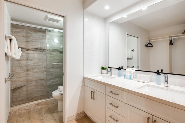 A bathroom with a glass shower enclosure, a white sink, a mirror, and a towel rack.