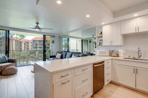 A modern kitchen with white cabinetry, a central island, and a view to a balcony with outdoor furniture.