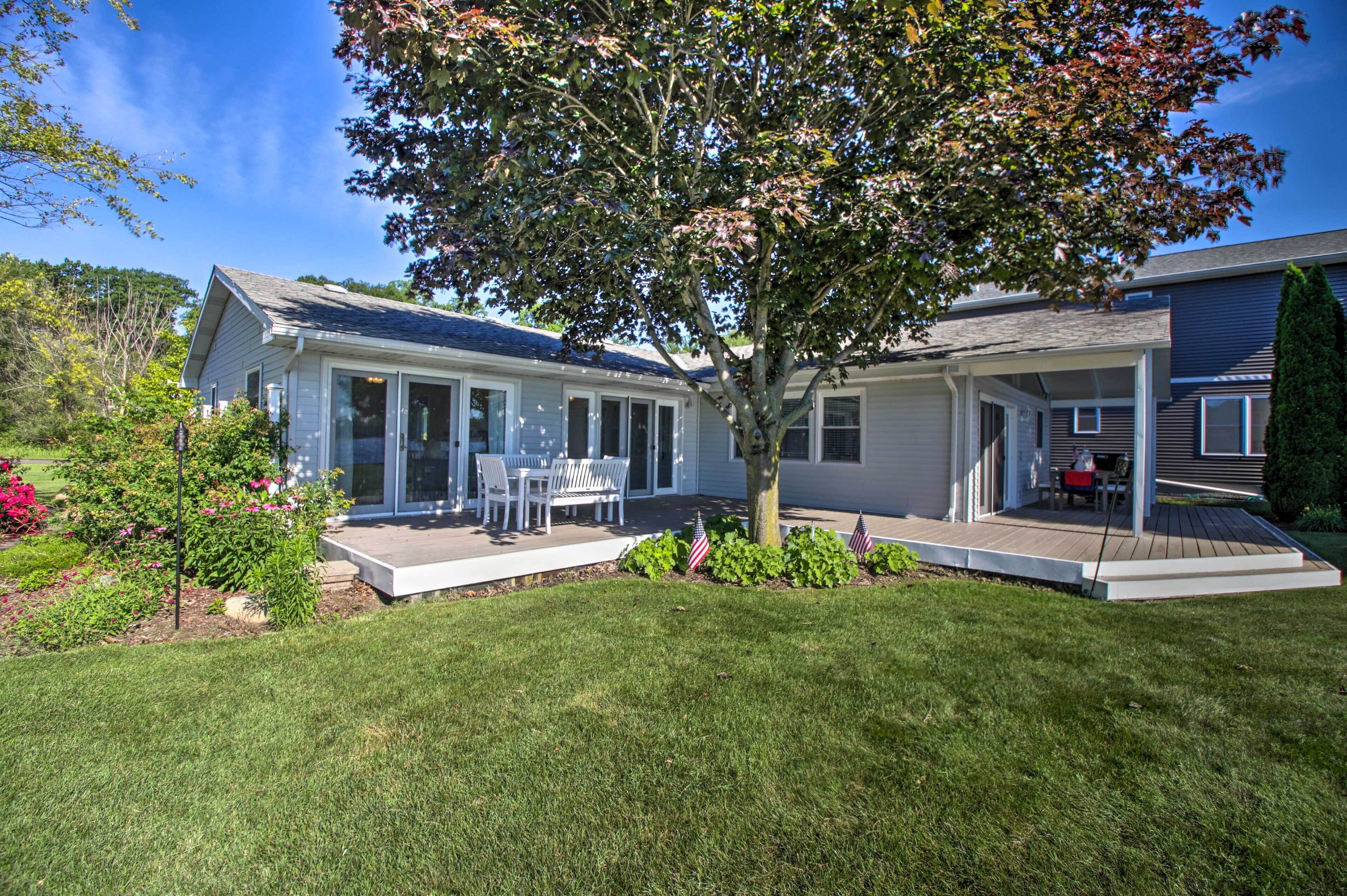 A two-story house with a covered patio, a lawn, and a tree.