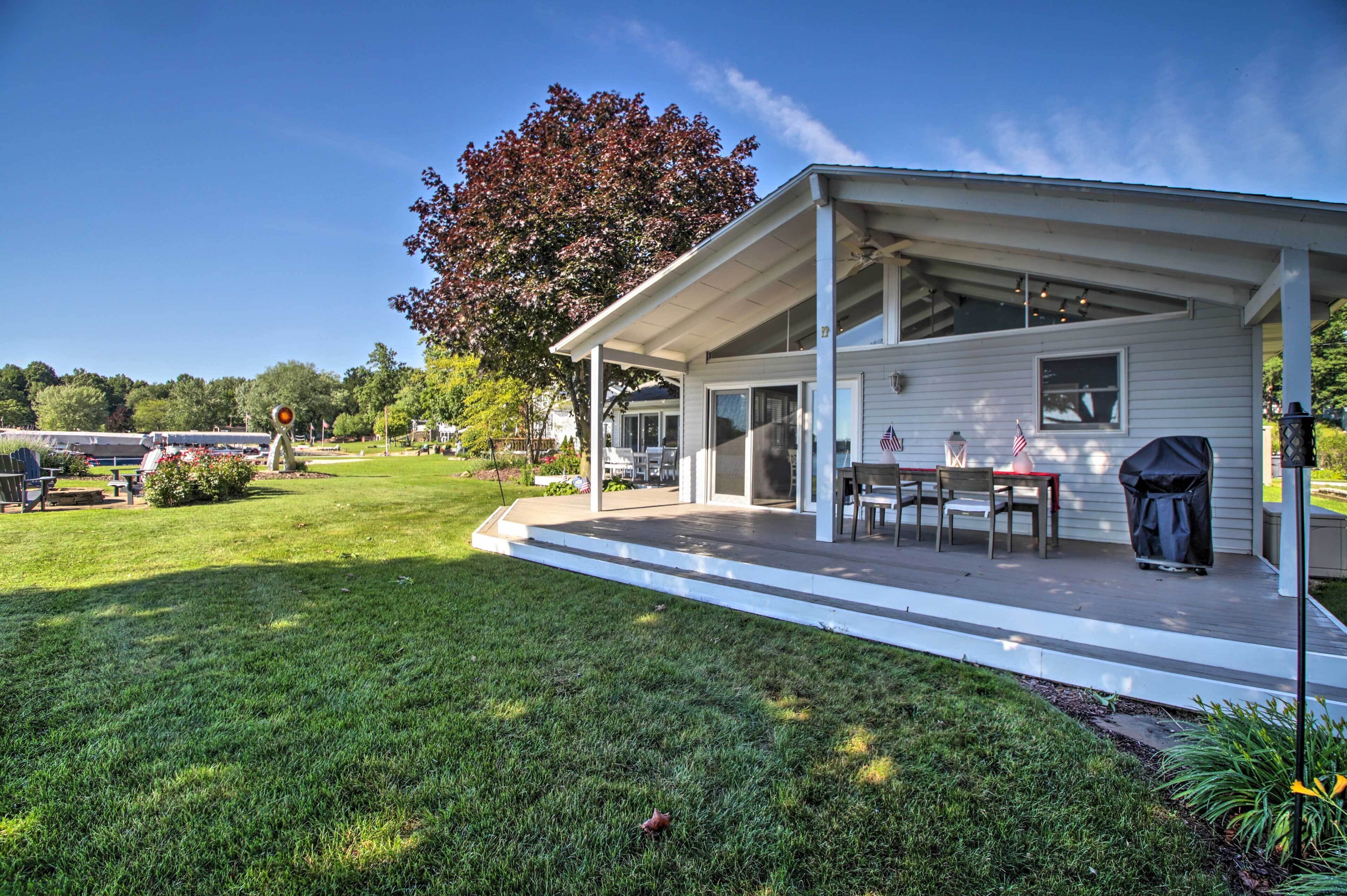 A covered outdoor patio with a table and chairs, a grill, and a lawn with a tree.