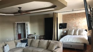 Une chambre d’hôtel moderne avec un canapé d’angle, un lit, un téléviseur à écran plat et un mur décoratif en briques.