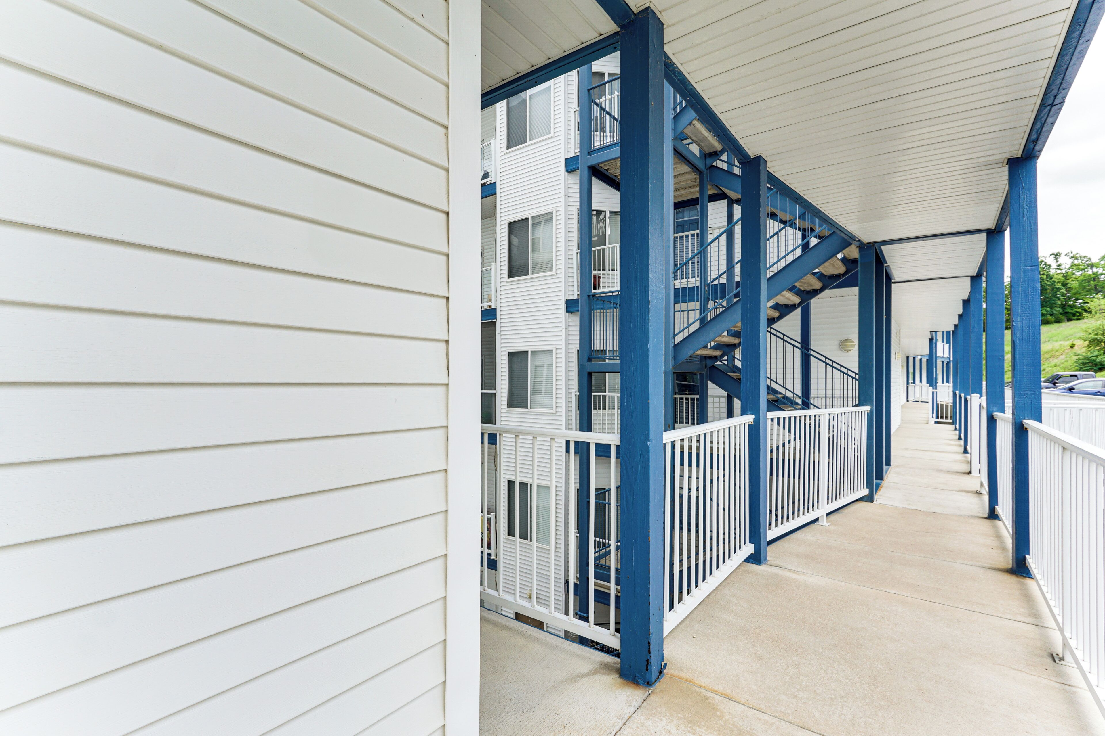 A covered outdoor area with a concrete floor, white railings, and blue structural supports.