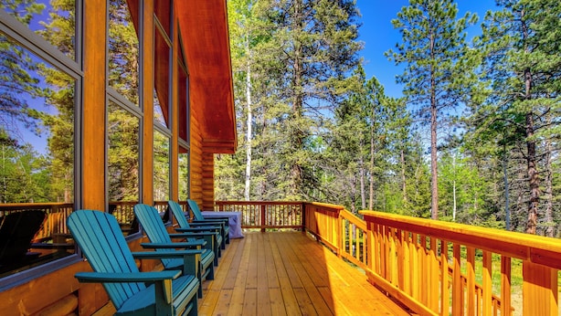 A wooden deck with Adirondack chairs, a wooden railing, and a view of a forest. - Sunny Forest Cabin w/ Views of Pikes Peak Mtn! (Florissant)