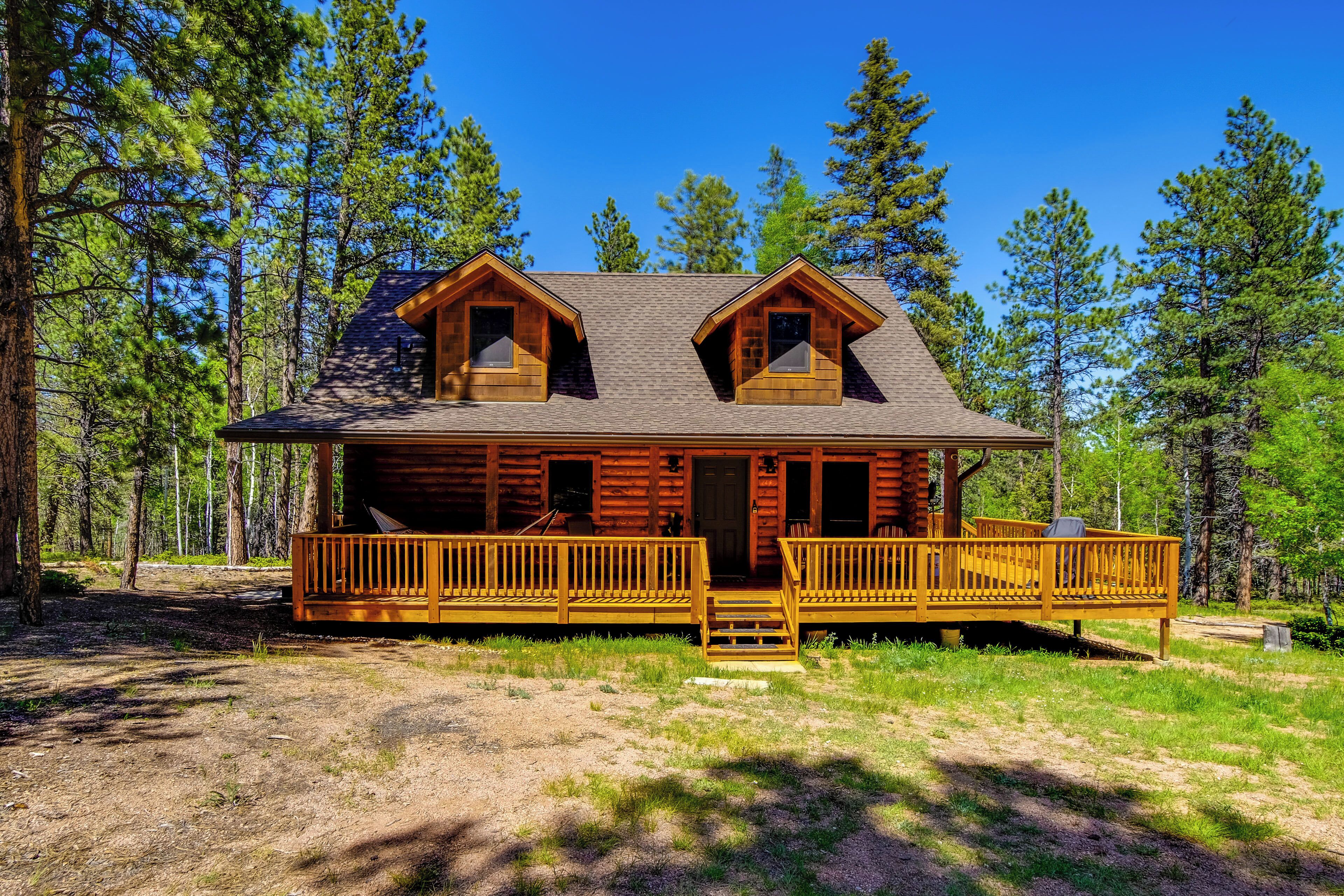 A log cabin with a front porch, two dormer windows, and a deck.