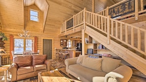 A log cabin interior with a wooden staircase, a dining area, a kitchen, and a living room with a sofa and a coffee table. - Sunny Forest Cabin w/ Views of Pikes Peak Mtn! (Florissant)