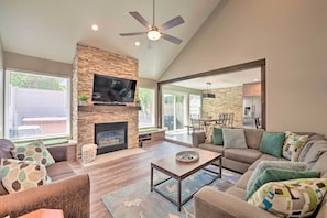 A spacious living room with a stone fireplace, a flat-screen TV, and a ceiling fan.