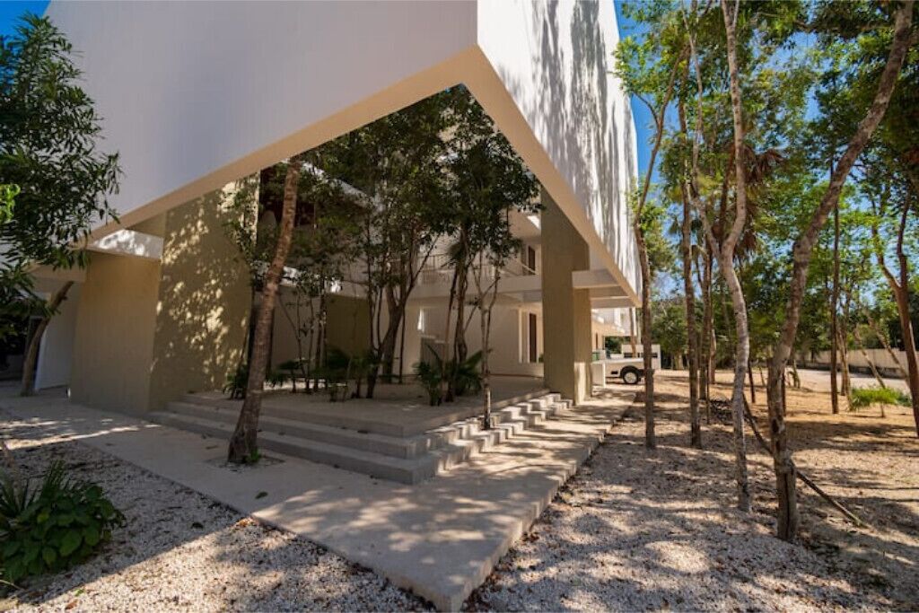 A modern building with a covered outdoor area, steps leading up to a door, and trees around the structure.