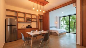 Una cucina moderna con frigorifero, microonde e mobili in legno. C'è un tavolo da pranzo con sedie e un letto con vista sulla finestra.