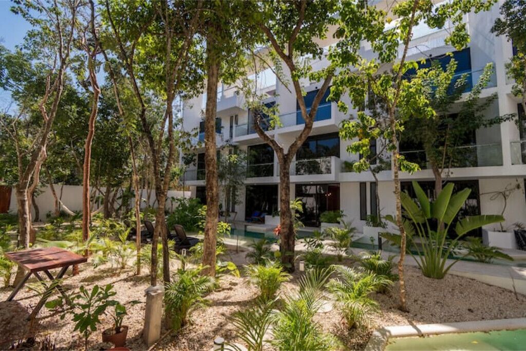 A modern building with multiple balconies, surrounded by lush greenery and trees.