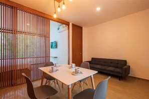 A modern room with a dining table set for four, a sofa, and a wooden partition with vertical slats. - Intimate apartment • Sak 206 (Tulum)