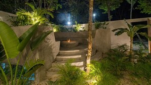Un espace extérieur aménagé pour la nuit, avec un foyer, des marches et des plantes tropicales.