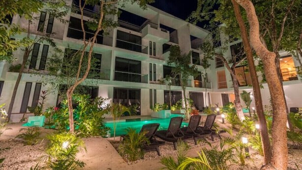 Un hôtel à plusieurs étages doté d’une piscine, d’un espace extérieur aménagé pour se détendre et d’un jardin luxuriant.
