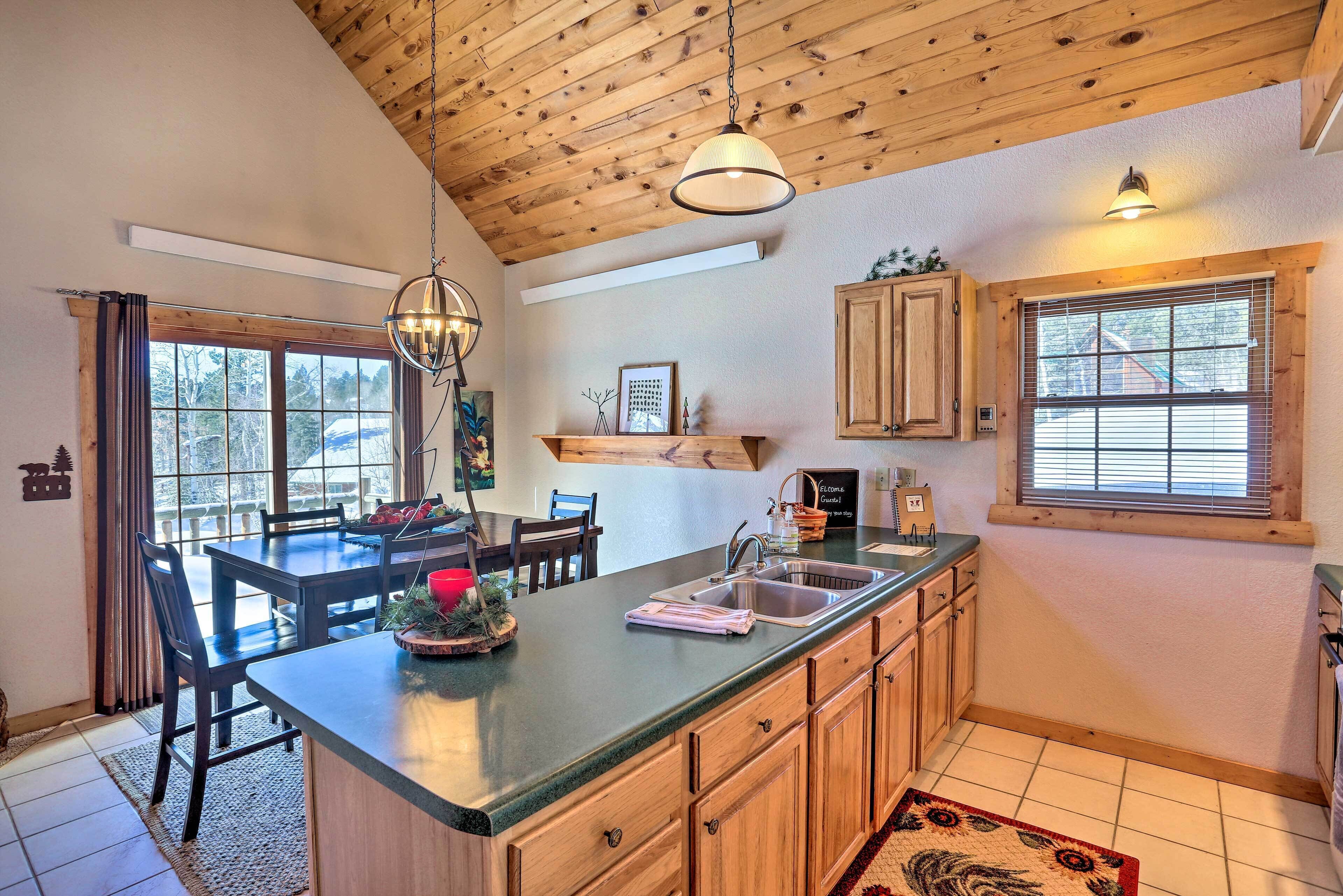 A kitchen with a large island, wooden cabinets, a hanging light fixture, and a window with blinds.