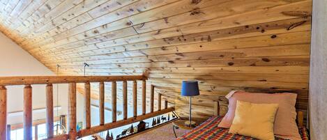 Eine Holzbalkendecke mit einem Bett, ausgestattet mit einer Karo-Bettdecke und einem Kissen.
