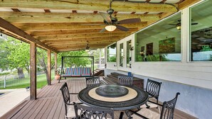 A covered outdoor patio with a round table and chairs, wooden beams, and a ceiling fan. - Waterfront Kingsland Home With Pool + River Access (Kingsland)