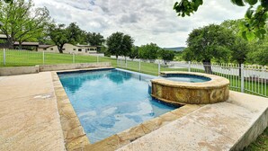 A rectangular swimming pool with a hot tub, surrounded by a white fence and greenery. - Waterfront Kingsland Home With Pool + River Access (Kingsland)