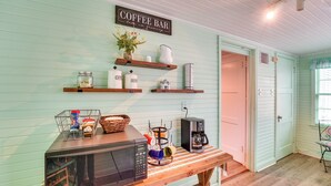 Eine Küche mit einer Kaffeebar-Beschilderung, einer Mikrowelle, einer Kaffeemaschine und verschiedenen Küchenutensilien in Regalen.