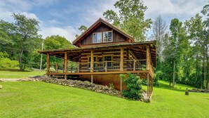 A wooden cabin with a balcony, surrounded by lush greenery and trees. - Stunning Creekside Cosby Cabin w/ Deck + Fire Pit! (Cosby)
