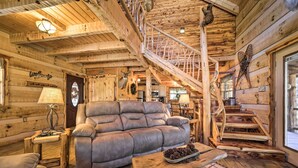 A cozy log cabin interior with a leather sofa, a wooden staircase, and rustic decor. - Stunning Creekside Cosby Cabin w/ Deck + Fire Pit! (Cosby)