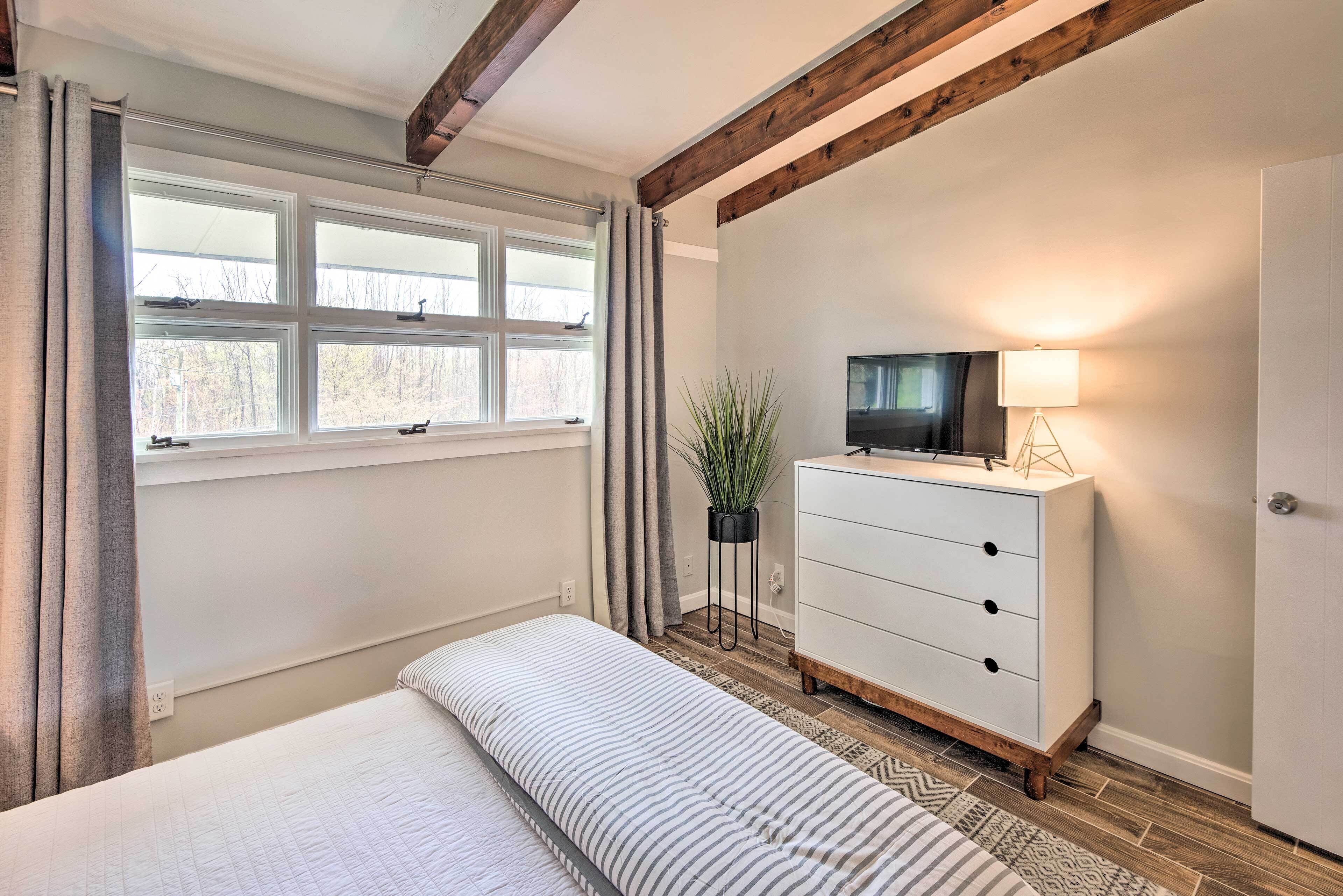 Ein Schlafzimmer mit Bett, Kommode, Fernseher und einem Fenster mit Vorhängen.