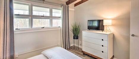 Ein Schlafzimmer mit Bett, Kommode, Fernseher und einem Fenster mit Vorhängen.