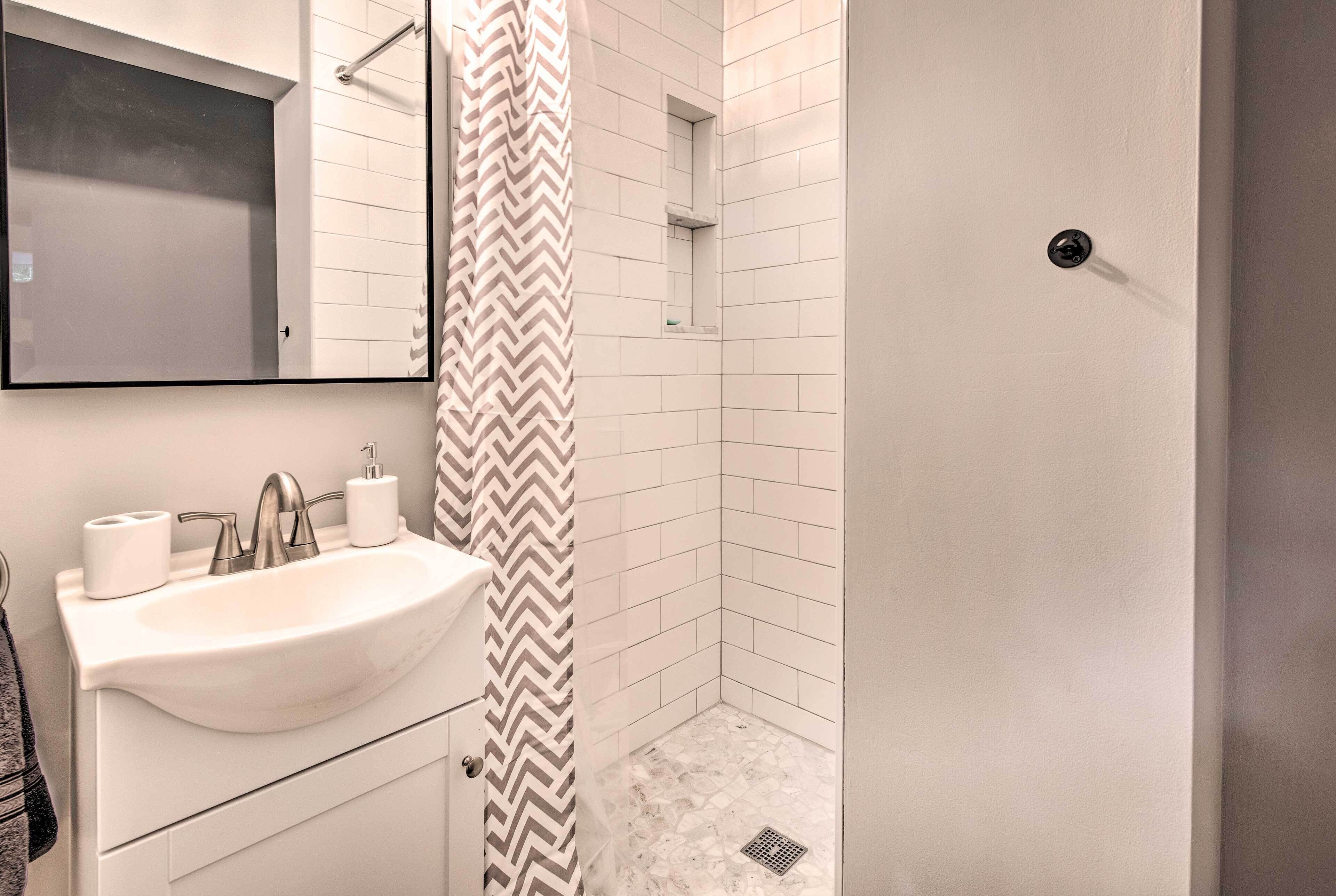 Un baño con lavamanos, espejo y ducha blancos.