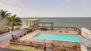 A wooden deck with a pool, lounge chairs, and a view of the ocean. - Waterfront Port Isabel Family Home w/ Pool & Pier! (Port Isabel)