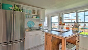 A modern kitchen with white cabinetry, a stainless steel refrigerator, a wooden island, and a view of the outdoors through large windows. - Waterfront Port Isabel Family Home w/ Pool & Pier! (Port Isabel)