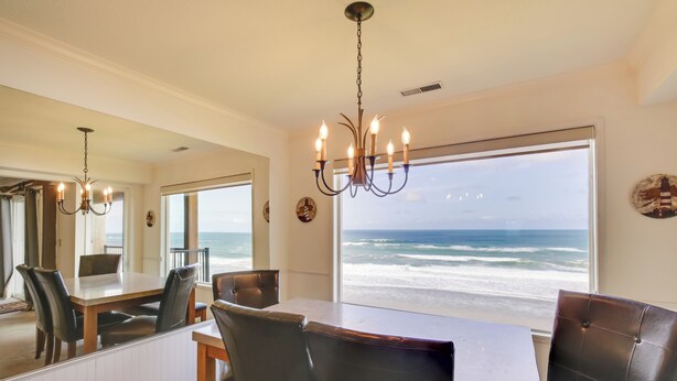 A dining area with a view of the ocean, a chandelier, and a large window. - Lincoln City Vacation Rental w/ Pool & Ocean Views (Gleneden Beach)