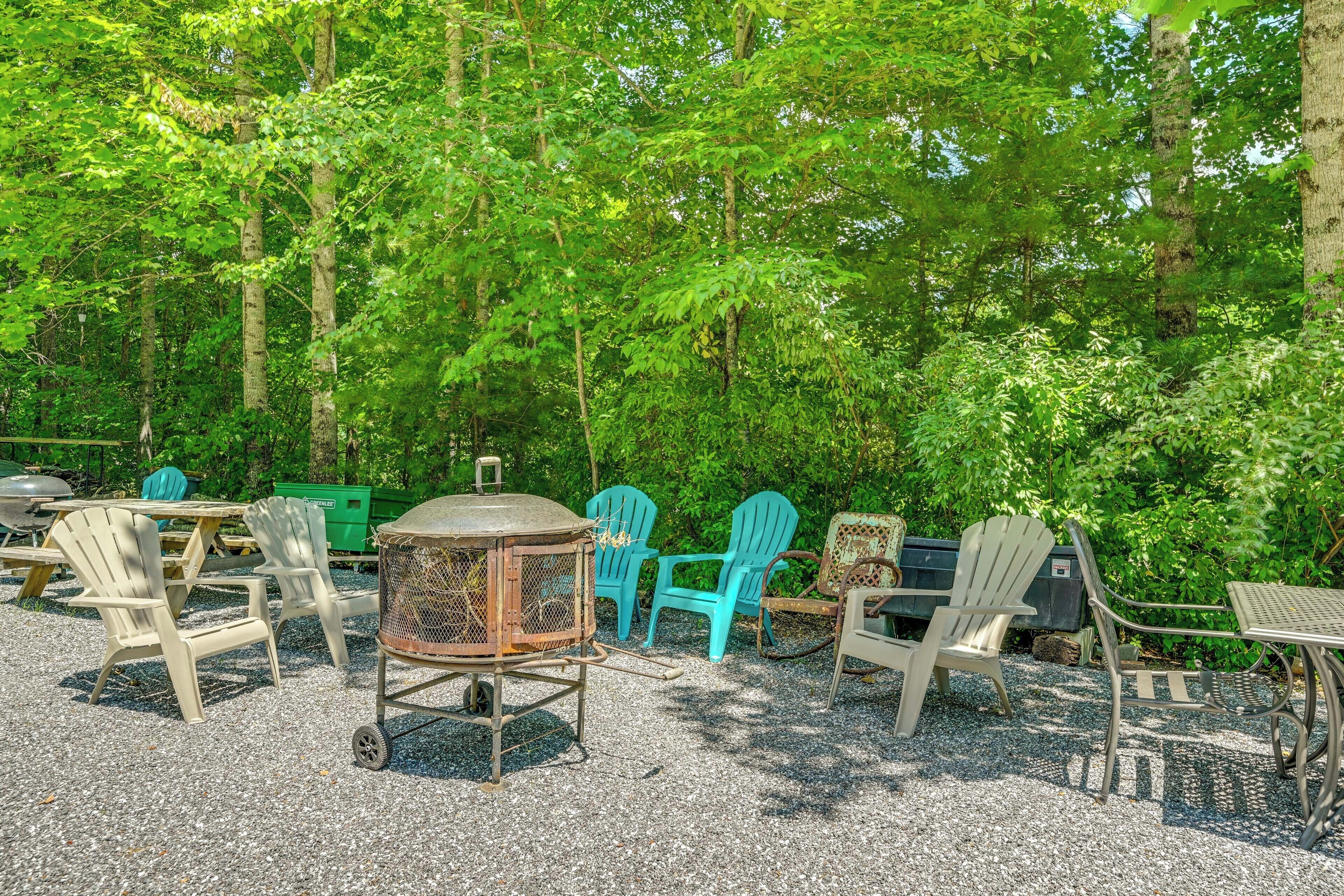 An outdoor seating area with Adirondack chairs and a metal table, surrounded by trees.