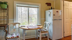 Une cuisine avec une fenêtre, un réfrigérateur, une table à manger avec des chaises et une plante suspendue.