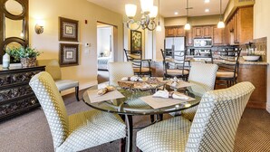 A dining area with a glass table surrounded by patterned chairs, a chandelier, and wooden cabinets in the background. - Branson Condo w/ Pool Access & Views, 3 Mi Dtwn! (Branson)