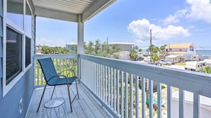 A covered balcony with a chair and table, overlooking a beach area with houses and parked cars. - Mexico Beach Home w/ Balcony - Steps to Beach (Port St. Joe)