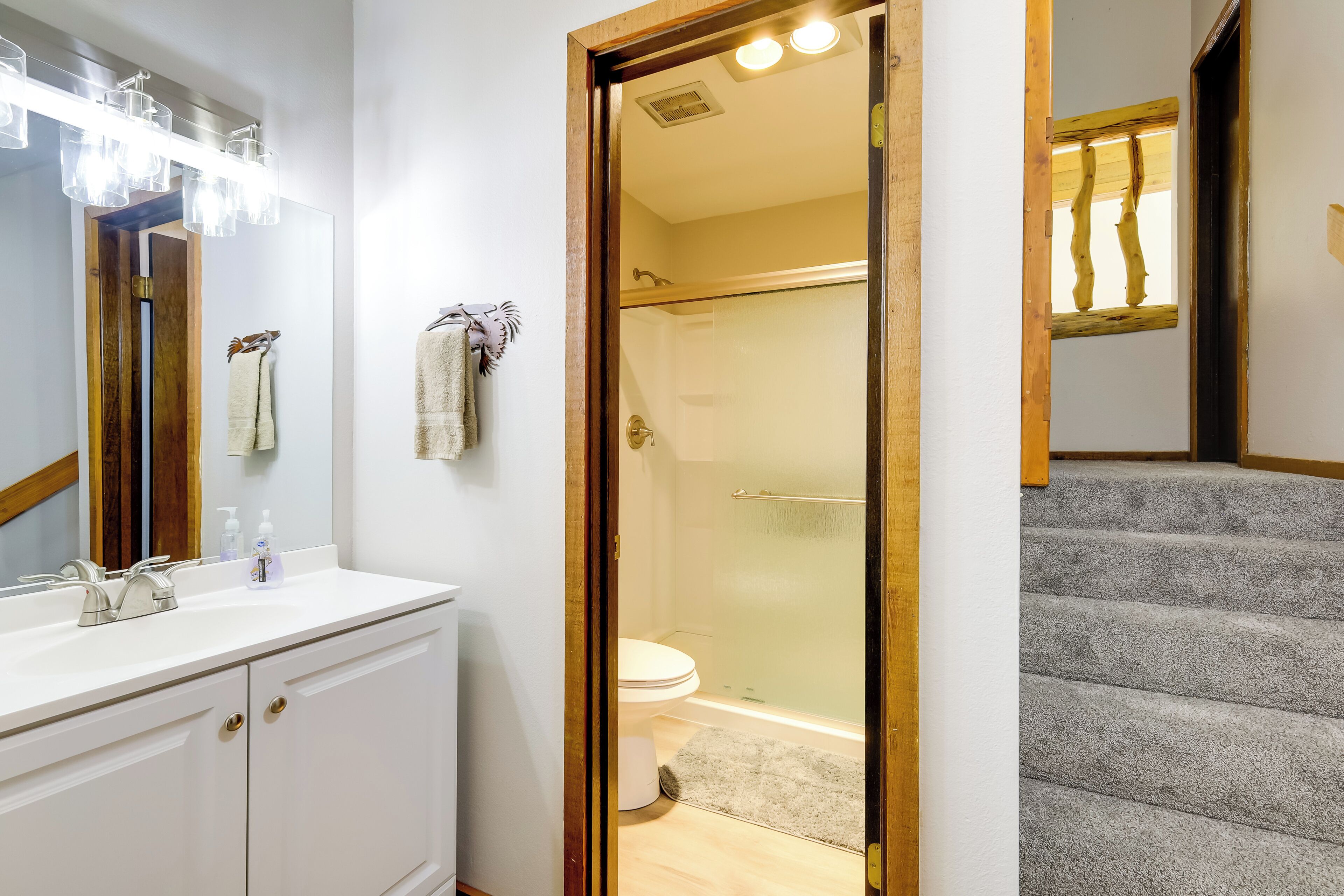 A bathroom with a white vanity, a glass shower enclosure, and a wooden staircase.