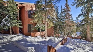 Una cabaña de madera con un porche cubierto de nieve y árboles circundantes.