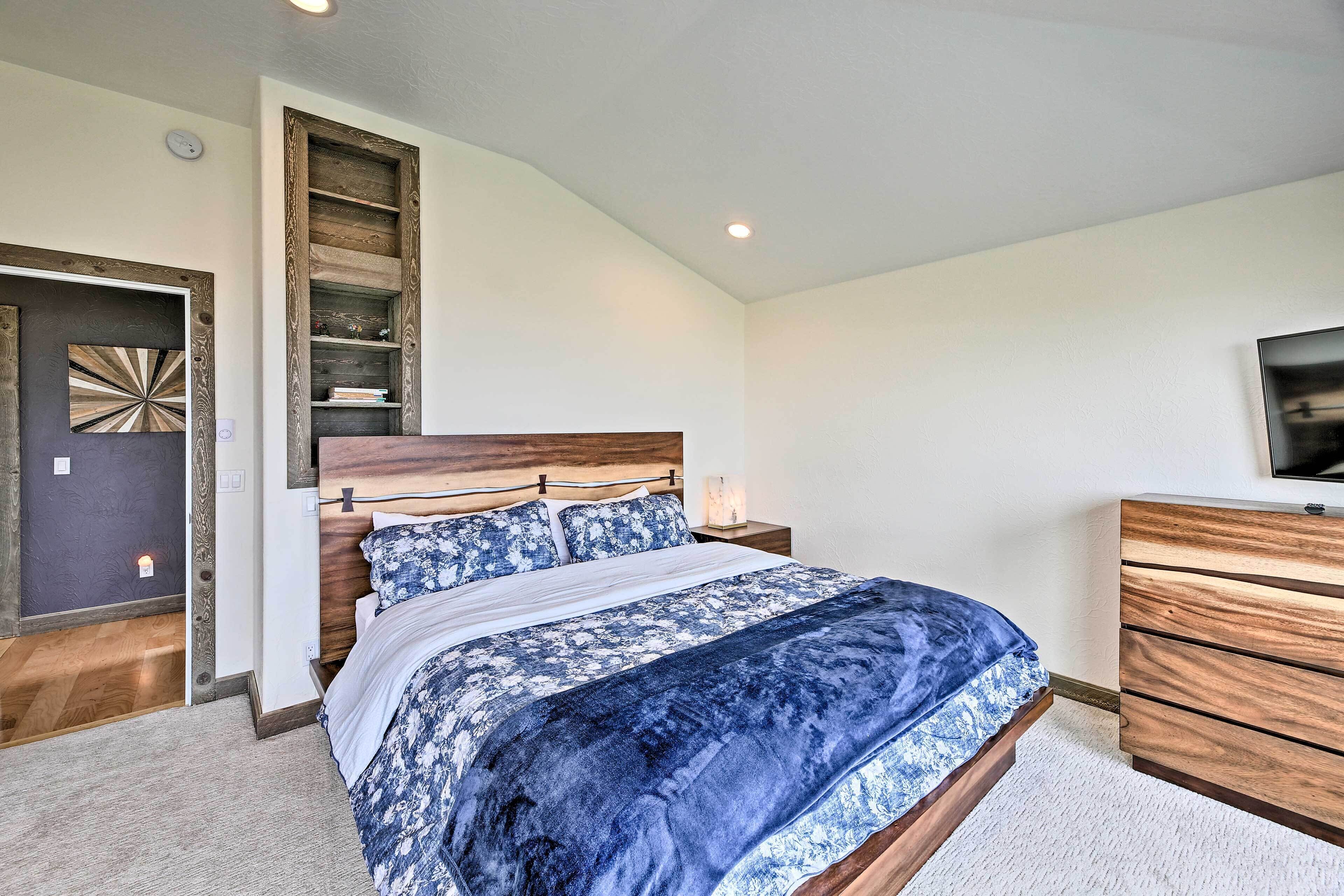 A bedroom with a bed, wooden headboard, bedside tables, a dresser, and a television on the wall.
