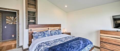 A bedroom with a bed, wooden headboard, bedside tables, a dresser, and a television on the wall.