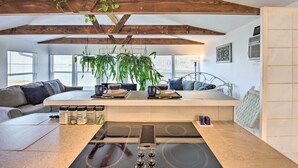Uma cozinha moderna com uma ilha central, vigas de madeira, plantas pendentes e fogão embutido.