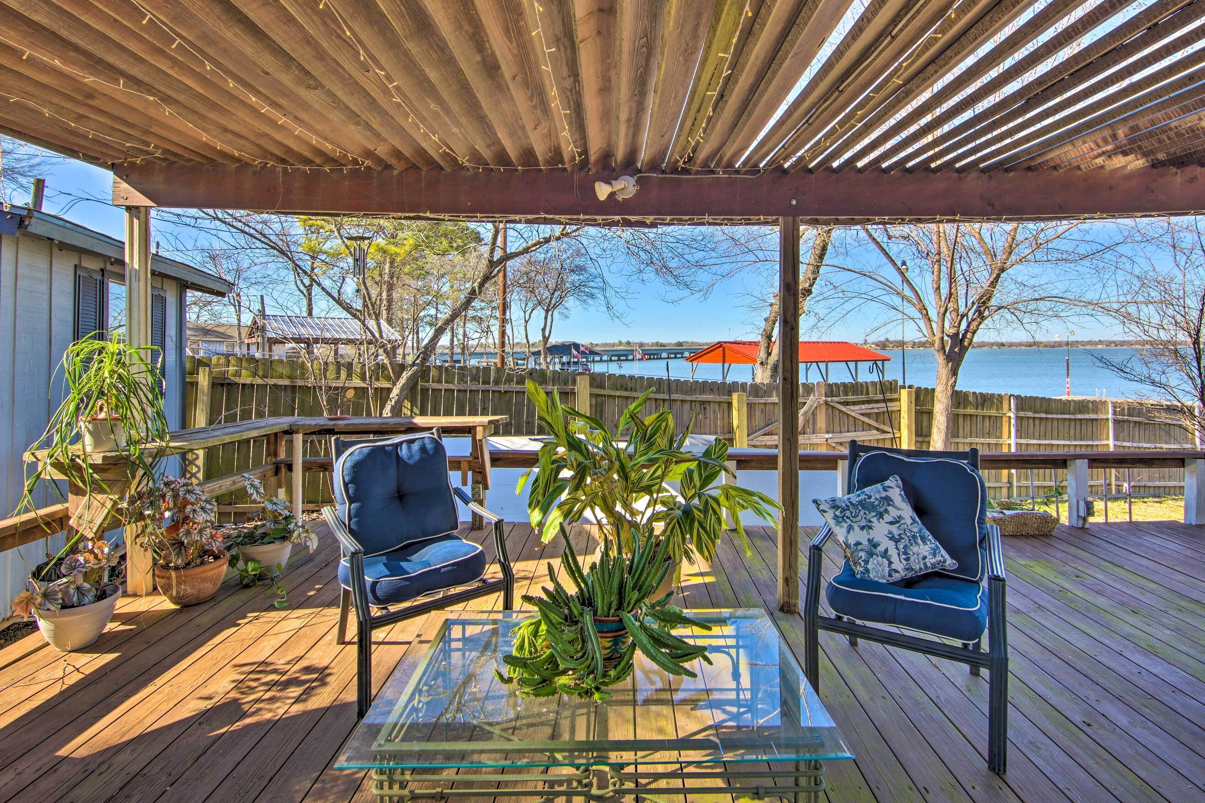 Une terrasse extérieure couverte, avec deux chaises, une table en verre et des plantes en pot.