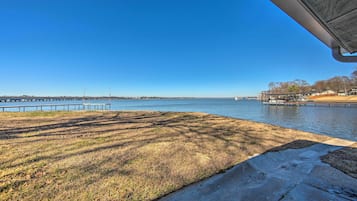 Vista al agua con un área verde, un sendero de concreto y un muelle que se adentra en el agua.