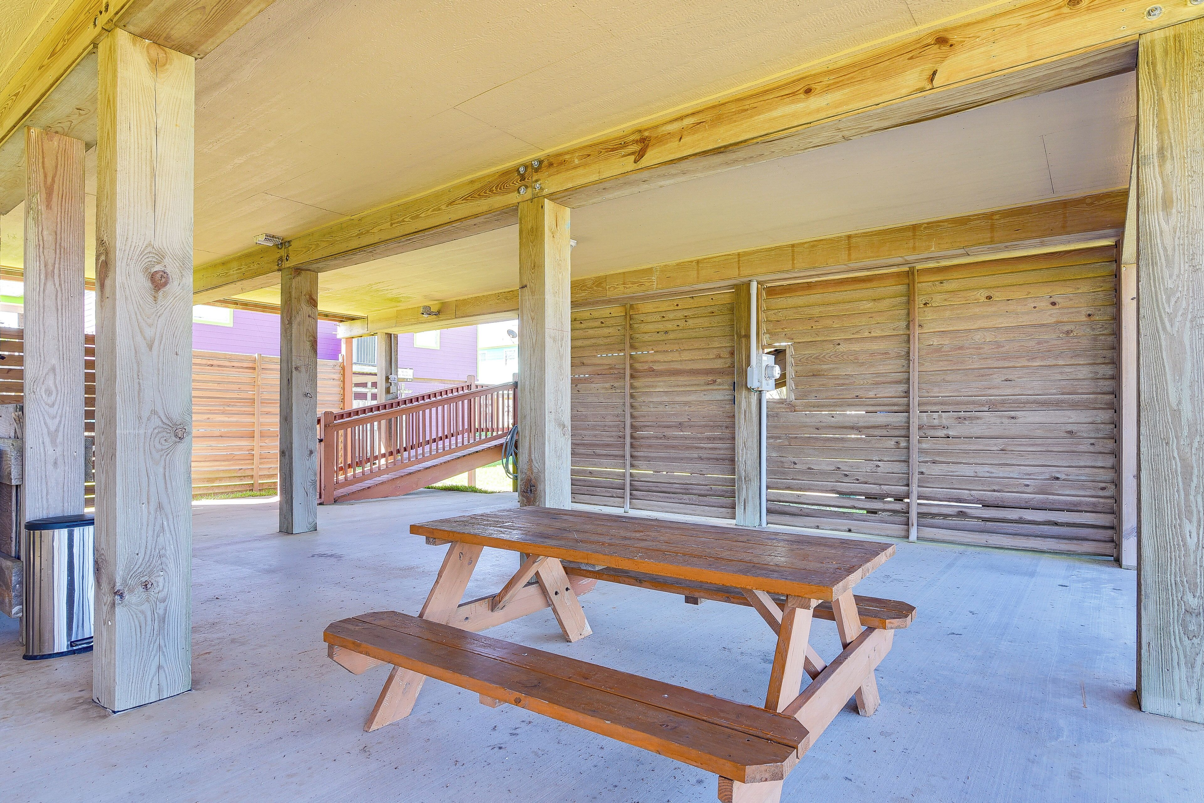 Un espace extérieur abrité, équipé d’une table de pique-nique et de bancs, de piliers en bois et d’une poubelle en métal.