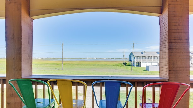A covered outdoor seating area with a view of a grassy field and a building in the distance. - Steps to Surfside Beach With Easy Ramp Access! (Freeport)